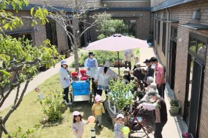 入居者が庭でレクリエーションや交流を楽しむ風景。日傘の下で団らんする様子